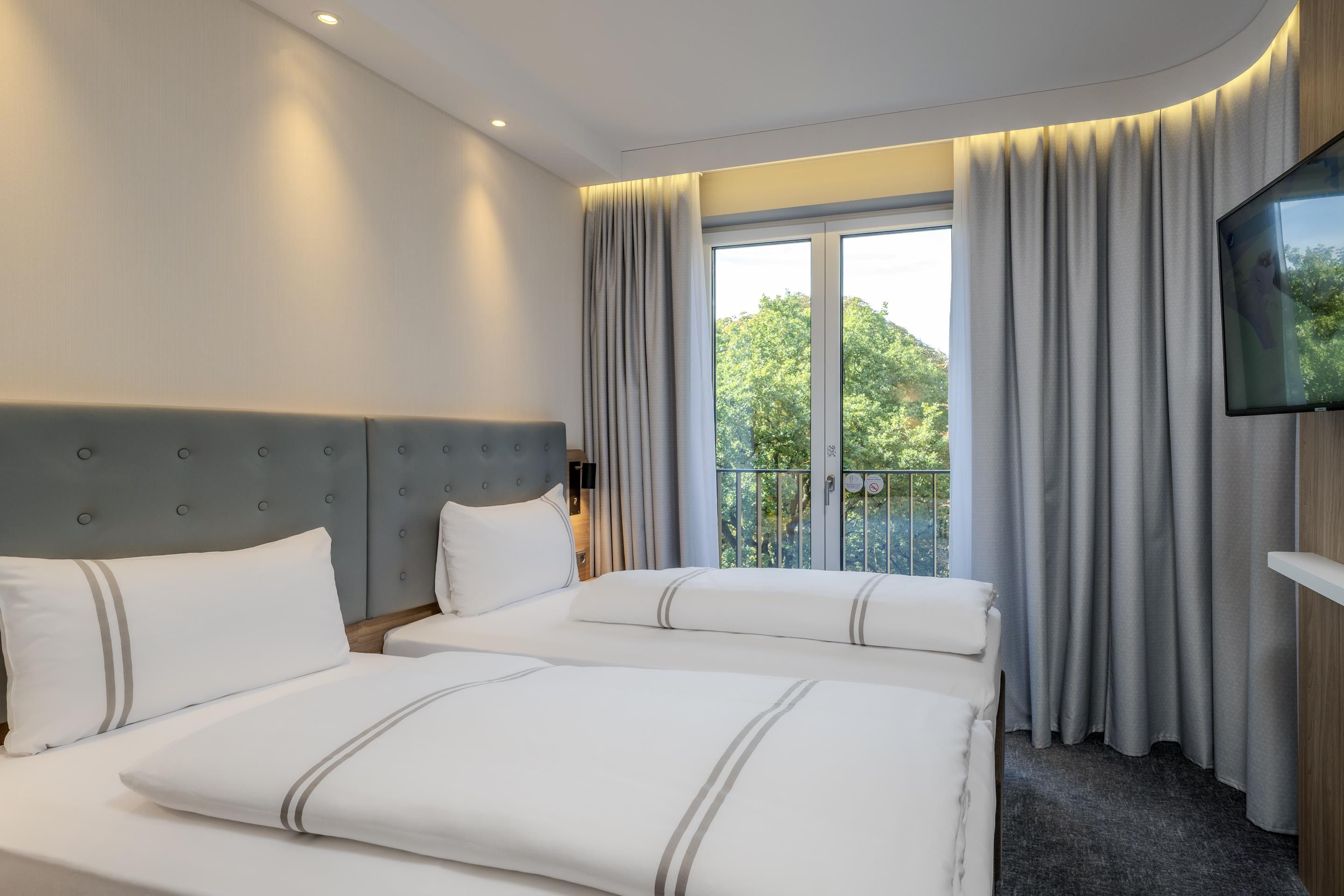 Une chambre d’hôtel avec deux lits, un téléviseur à écran plat et un balcon avec des rideaux.