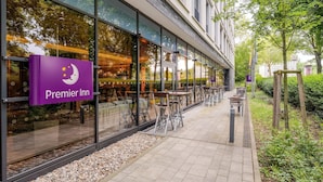 A Premier Inn hotel exterior with large windows, outdoor seating, and a gravel pathway.