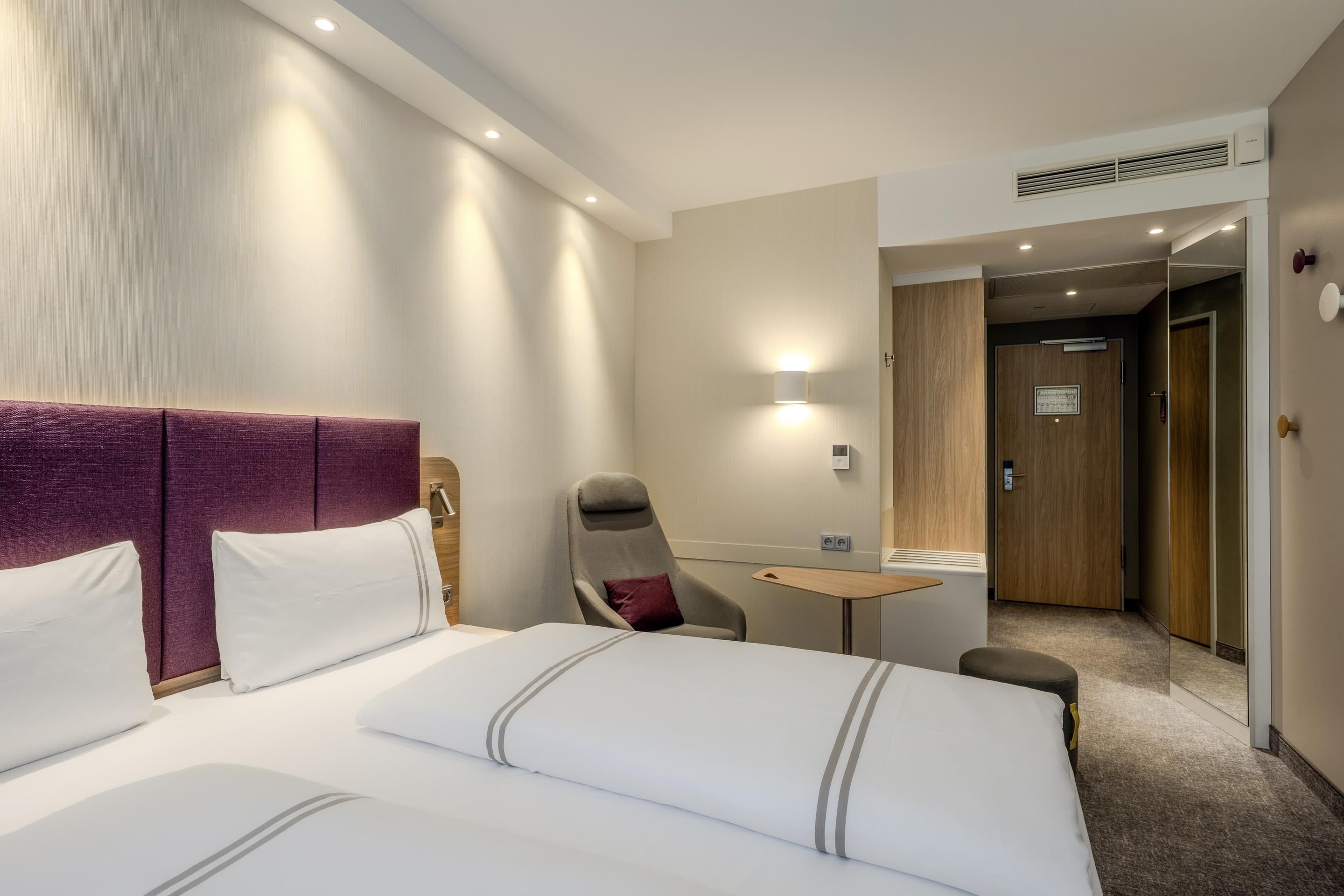 Ein Hotelzimmer mit einem großen Bett, einem Sessel, einem kleinen Tisch und einer Tür zu einem weiteren Raum.