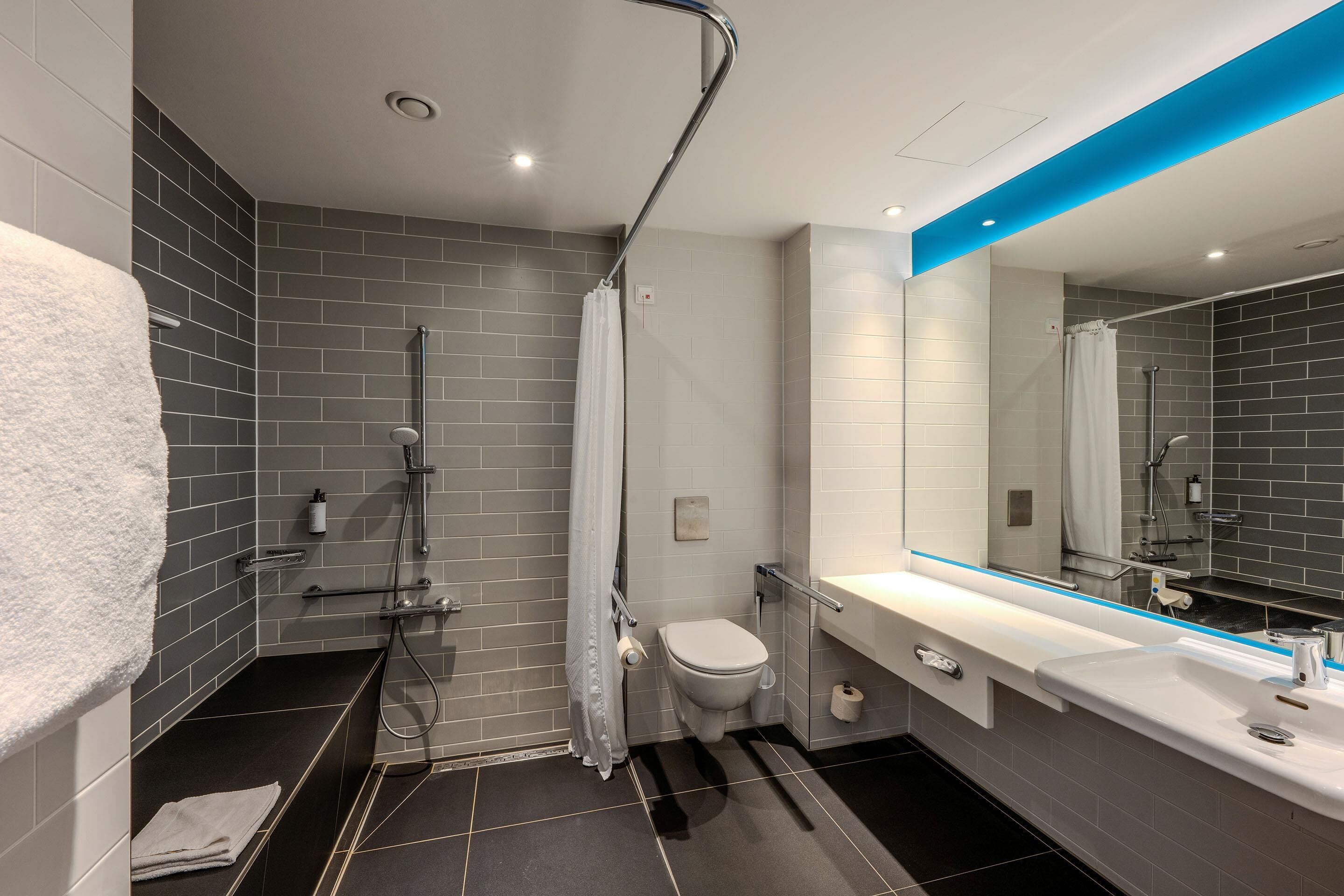 A modern bathroom with a shower, toilet, and sink, featuring grey tiles and a blue accent wall.