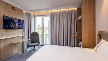 Une chambre d’hôtel équipée d’un lit, d’un bureau, d’une chaise, d’un téléviseur fixé au mur et offrant une vue sur l’extérieur.
