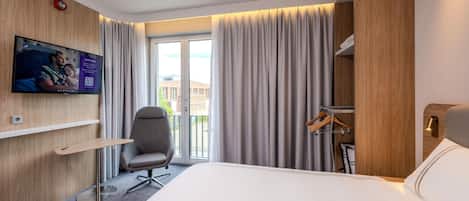 Habitación de hotel con cama, escritorio, silla, televisión montada en la pared y vista al exterior.