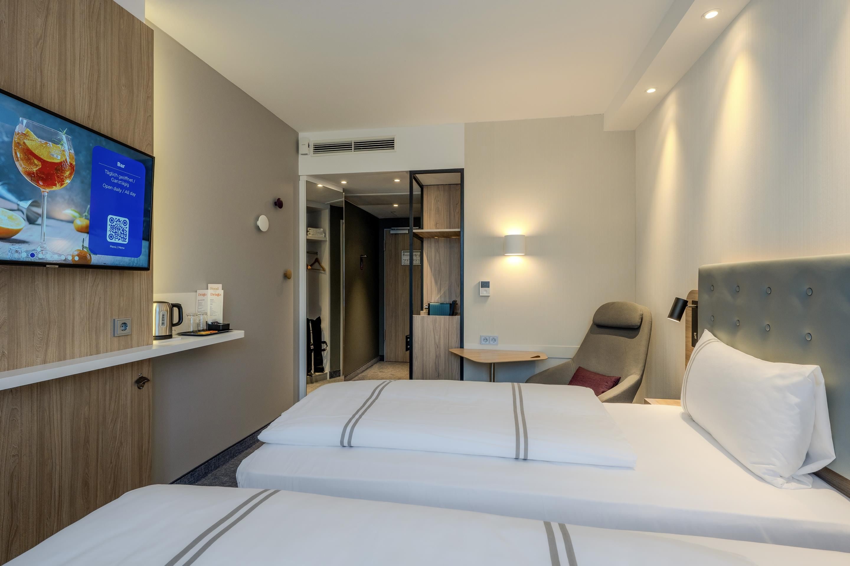 A hotel room with two beds, a TV on the wall, a small table, and a chair.
