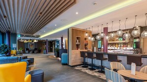 Een moderne hotellobby met een bar, zitplaatsen en een receptiebalie.