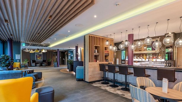 A modern hotel lobby with a bar area, seating arrangements, and a reception desk.
