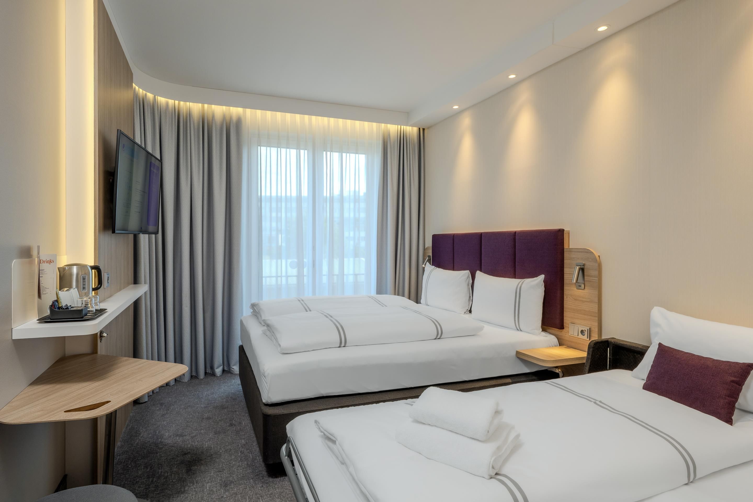 A hotel room with two beds, a TV, a coffee machine, and a window with curtains.