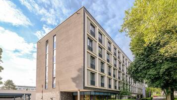 Un edificio moderno con fachada plana, grandes ventanales y una calle arbolada.