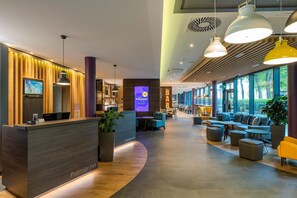 A modern hotel lobby with a reception desk, seating area, and large windows.