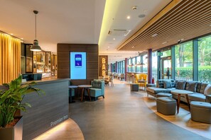A modern hotel lobby with a reception desk, seating area, and large windows.