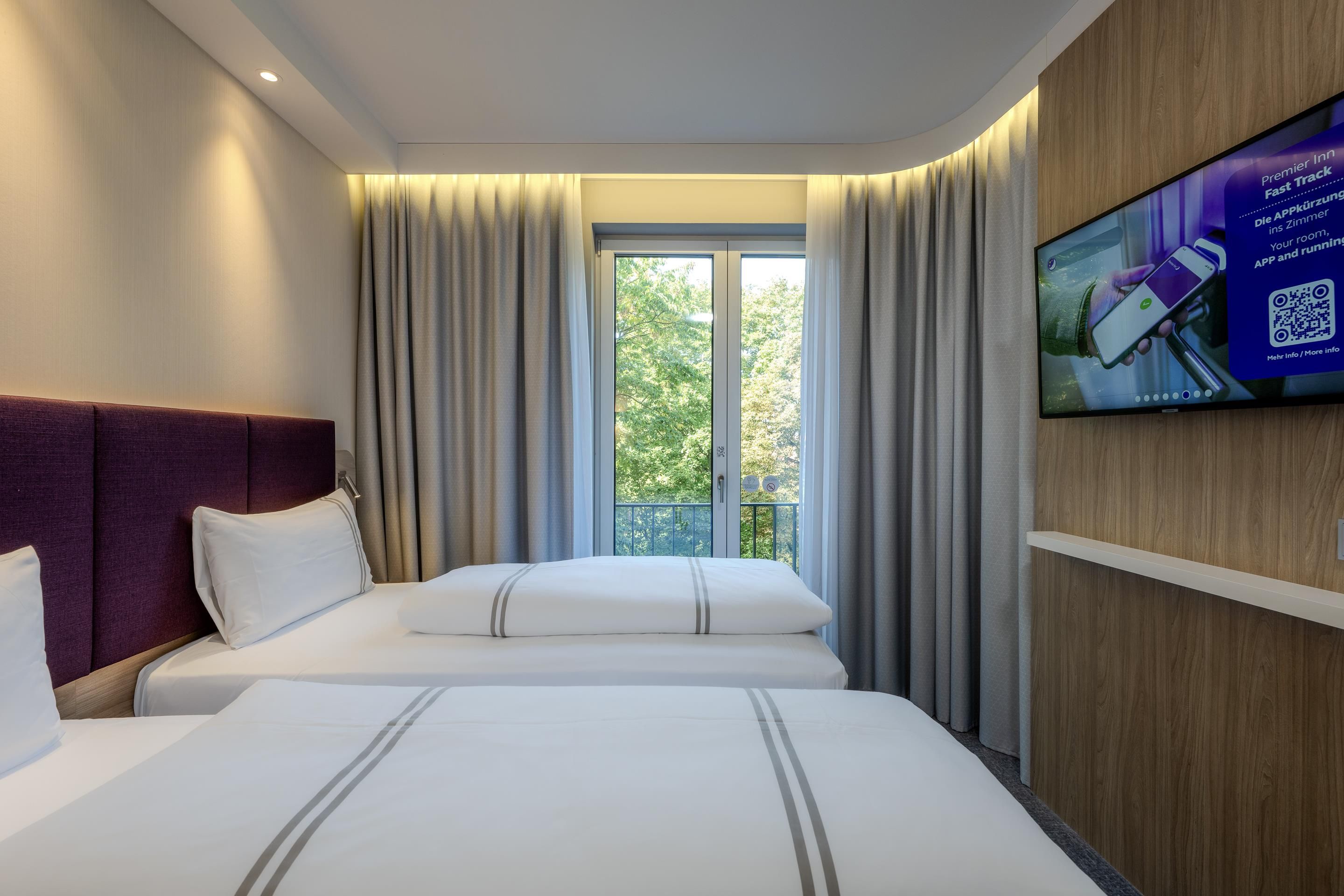 A hotel room with two beds, a TV on the wall, and a window with curtains.