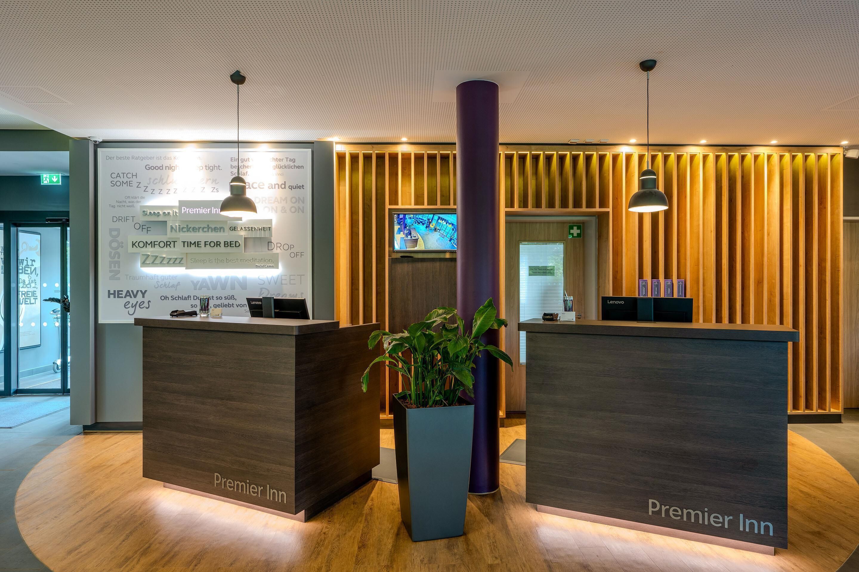 A hotel reception area with two reception desks, a large potted plant, and a television screen.