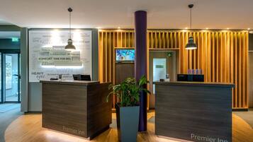 A hotel reception area with two reception desks, a large potted plant, and a television screen.