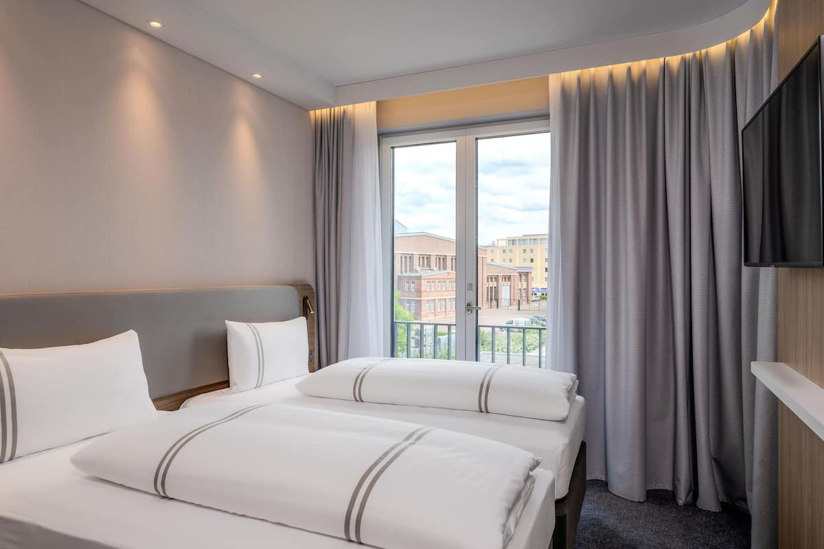 Une chambre d’hôtel avec un grand lit, une télévision à écran plat, un balcon avec des rideaux et une vue sur les immebles.