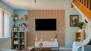 Un soggiorno moderno con televisione, divano, tavolino e libreria.