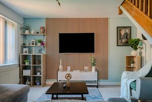 Ein modernes Wohnzimmer mit Fernseher, einer Couch, einem Couchtisch und einem Bücherregal.