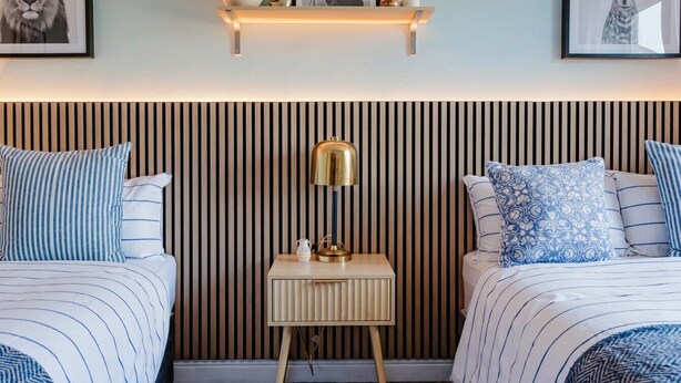 Una camera da letto con due letti, un comodino con una lampada, una mensola a parete e un tappeto decorato.
