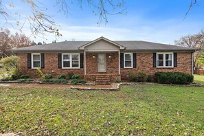 A single-story brick house with a front porch, a front door, and a small front yard. - New Cozy / Near MTSU / Getaway ~ Sleeps 8+ (Murfreesboro)