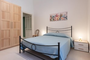 Ein Schlafzimmer mit einem Bett, einem Nachttisch, einem Holzschrank und einer Tür zu einem anderen Raum.