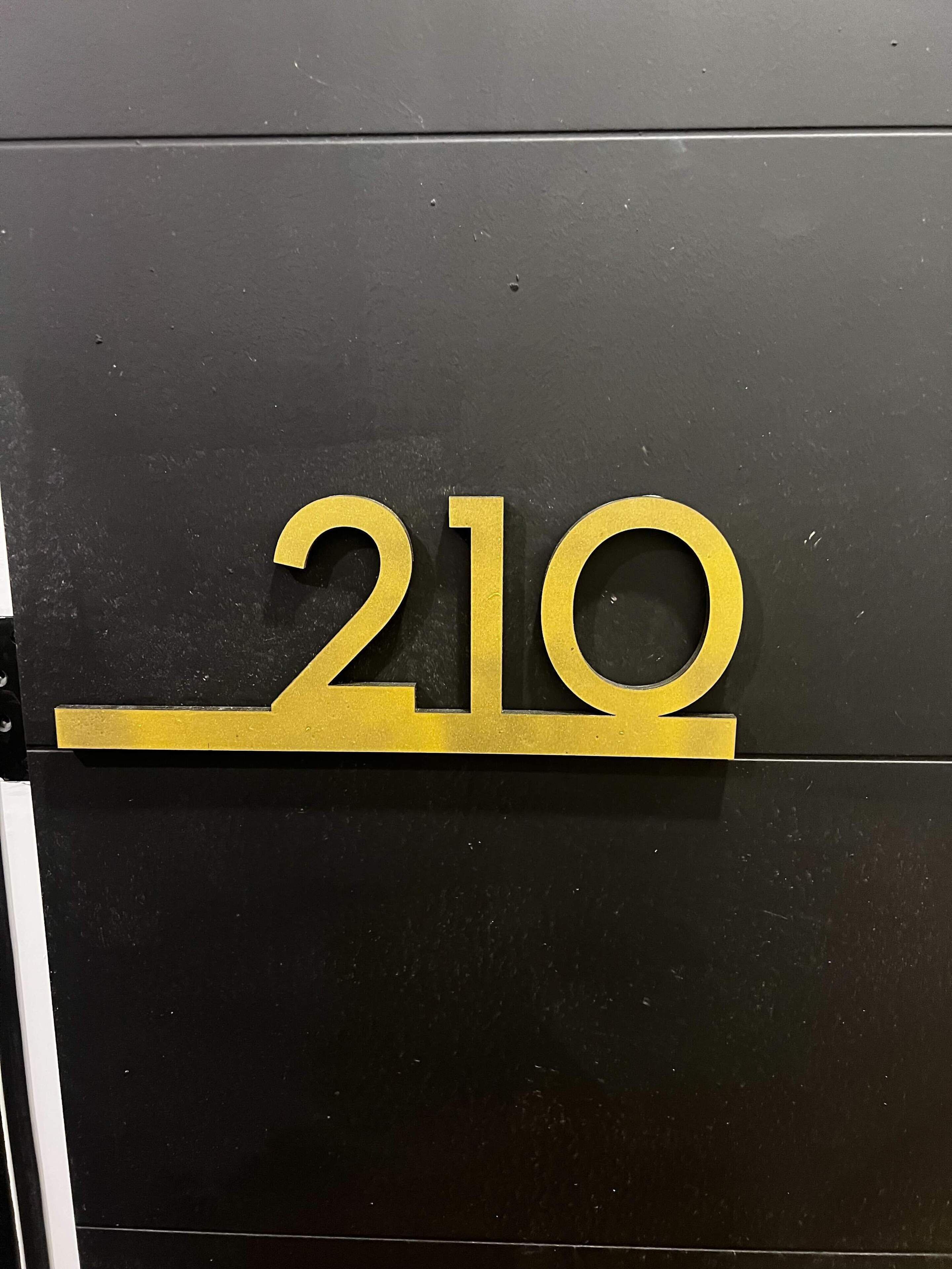 A black wall with a gold number '210' sign.