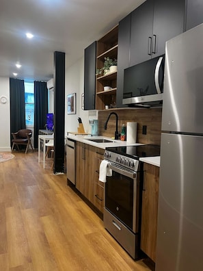 A modern kitchen with wooden cabinets, a stainless steel refrigerator, a built-in oven, and a microwave. - Sunbird Studio, Bright Downtown Escape, AC (Halifax)