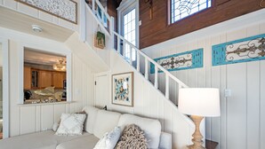 A staircase with white railings, a white sofa with decorative pillows, a lamp, and wall art.