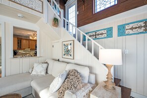 A staircase with white railings, a white sofa with decorative pillows, a lamp, and wall art.