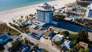 An aerial view of a coastal hotel with a central tower, beachfront, and surrounding buildings.