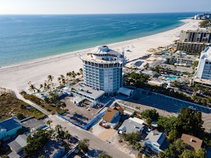 An aerial view of a coastal hotel with a central tower, beachfront, and surrounding buildings.