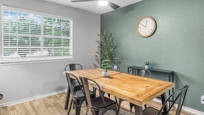 Un coin repas avec une table en bois, des chaises noires, une plante en pot, une horloge murale et un ventilateur de plafond.