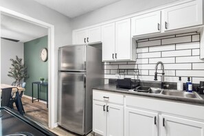 Una cocina moderna con armarios blancos, un refrigerador de acero inoxidable, un lavamanos con grifo y un reloj en la pared.