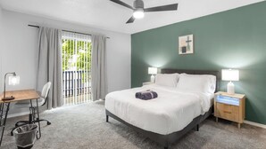 Une chambre d’hôtel comprenant un lit, des tables de chevet, un bureau, une chaise, un ventilateur de plafond et une vue sur l’extérieur par une fenêtre.