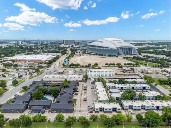 Vista aérea de un estadio con un amplio estacionamiento, rodeado de edificios y zonas verdes.