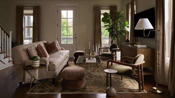 A living room with a sofa, ottoman, coffee table, chairs, a TV, and a large plant. - New Luxe East Nashville Home • Sleeps 6 Near DWTN (Nashville)