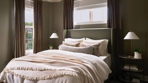 A bedroom with a large bed, two bedside lamps, a chandelier, and a view of a building through the window. - New Luxe East Nashville Home • Sleeps 6 Near DWTN (Nashville)