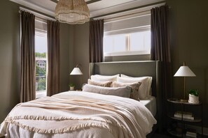 A bedroom with a large bed, two bedside lamps, a chandelier, and a view of a building through the window. - New Luxe East Nashville Home • Sleeps 6 Near DWTN (Nashville)