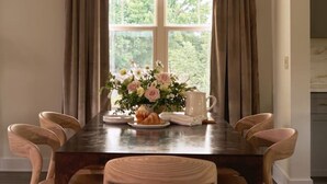 A dining room with a wooden table, six chairs, a chandelier, a window with curtains, and a vase with flowers. - New Luxe East Nashville Home • Sleeps 6 Near DWTN (Nashville)