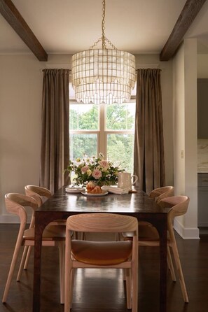 A dining room with a wooden table, six chairs, a chandelier, a window with curtains, and a vase with flowers. - New Luxe East Nashville Home • Sleeps 6 Near DWTN (Nashville)