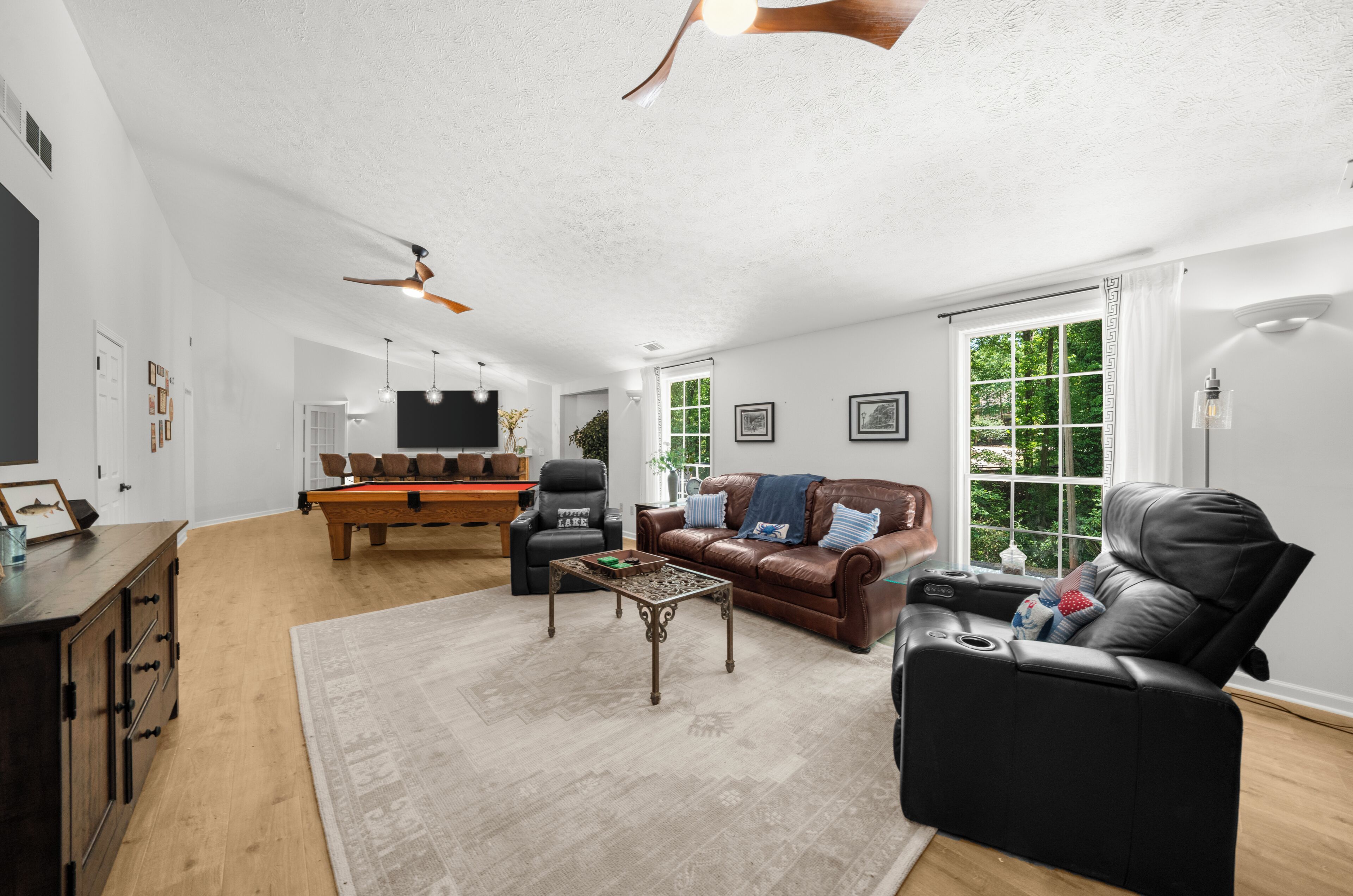 Ein Wohnzimmer mit Billardtisch, Ledersofas, Relaxsesseln und Deckenventilator.