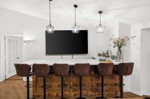 A bar area with a white countertop, six bar stools, and three hanging pendant lights. - Fantastic 6 bedroom house with Deep water on Lake Lanier (Gainesville)