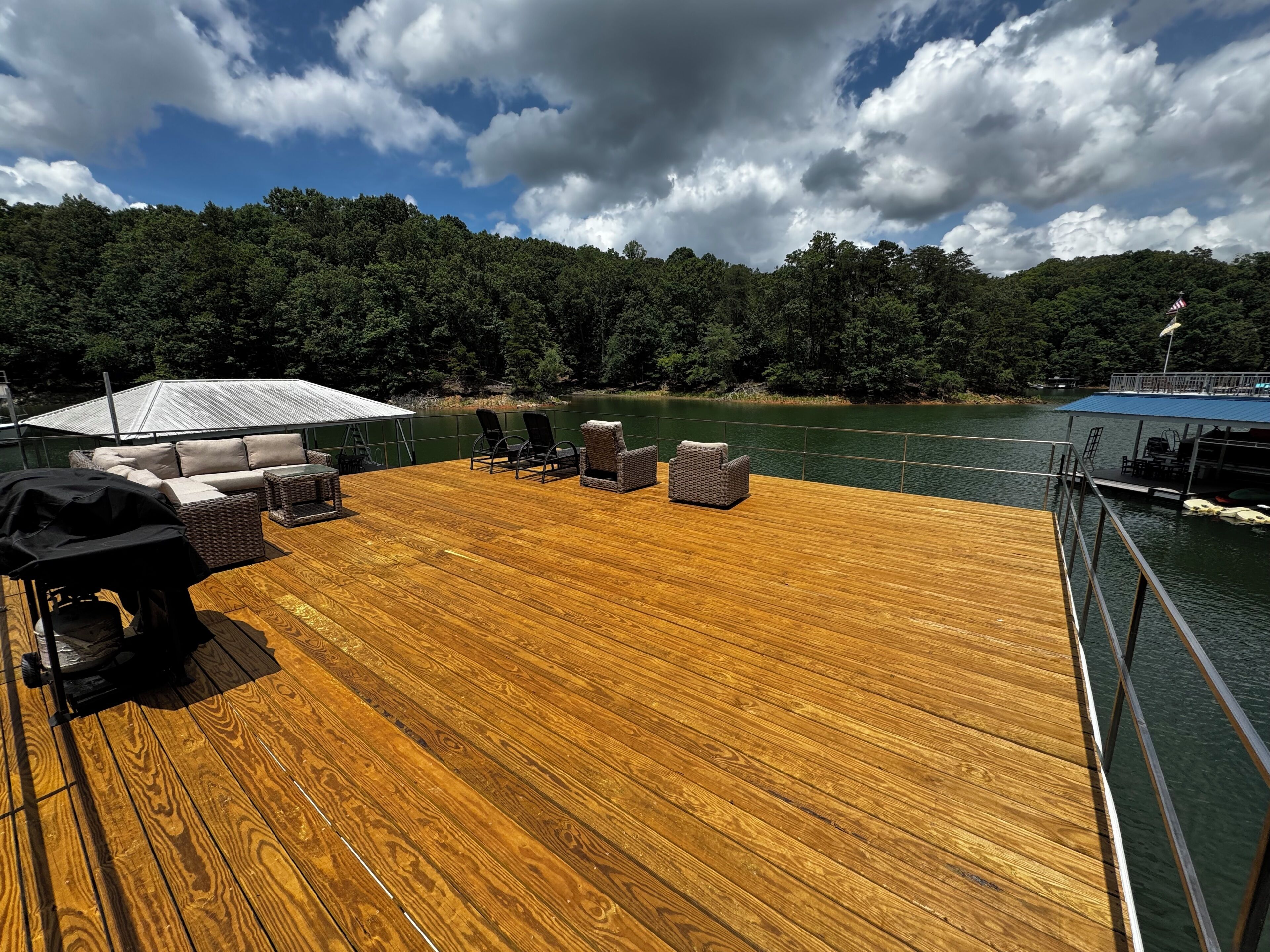A wooden deck with outdoor furniture, a covered area, and a view of a lake surrounded by trees.