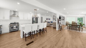 Una cocina moderna con armarios blancos, una estufa de acero inoxidable y una zona de comedor con una mesa y sillas de madera.