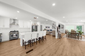 Una cocina moderna con armarios blancos, una estufa de acero inoxidable y una zona de comedor con una mesa y sillas de madera.