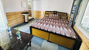 A room with a bed, a small table with bottles, a sink, and a window with curtains.