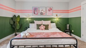 Een slaapkamer met een bed, groene wanden, een plant, ingelijste foto's en een nachtkastje.