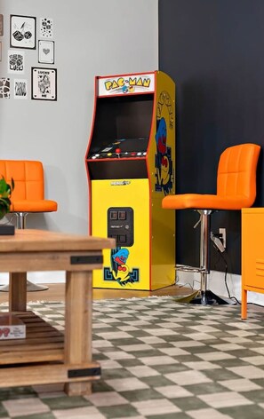 A Pac-Man arcade machine in a room with orange chairs and a checkered floor.