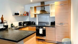A modern kitchen with a central island, built-in oven, stainless steel range hood, and wooden cabinets. - Boutique apartment near Old Trafford · terrace · sleeps 6 (Greater Manchester)