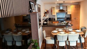 A modern kitchen with a central island, dining area with white chairs, and a striped wall design. - Boutique apartment near Old Trafford · terrace · sleeps 6 (Greater Manchester)