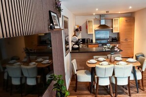 A modern kitchen with a central island, dining area with white chairs, and a striped wall design. - Boutique apartment near Old Trafford · terrace · sleeps 6 (Greater Manchester)