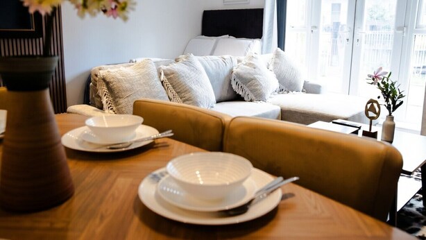 A modern living room with a sofa, a dining table with plates and cutlery, a vase with flowers, and a window with a view of buildings. - Boutique apartment near Old Trafford · terrace · sleeps 6 (Greater Manchester)