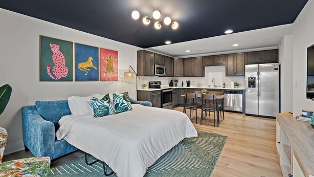 A modern apartment with a bed, blue sofa, kitchen, and artwork on the wall. - NEW ~ Charming, Cozy Apt DWTN Murfreesboro, TN (Murfreesboro)